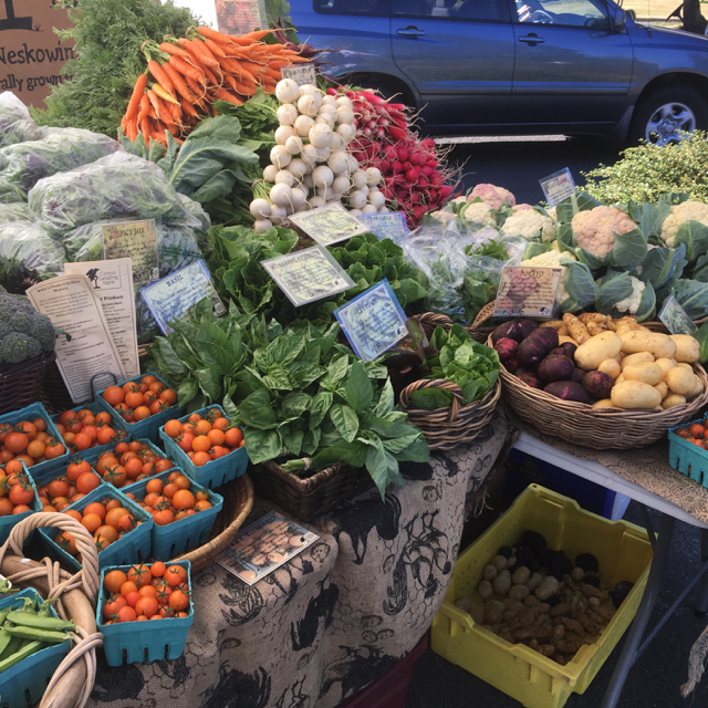 Gemüsestand auf einem Markt mit buntem Angebot: Tomaten, Karotten, Radieschen, Salat, Kartoffeln und Kräuter in Körben und Kisten.